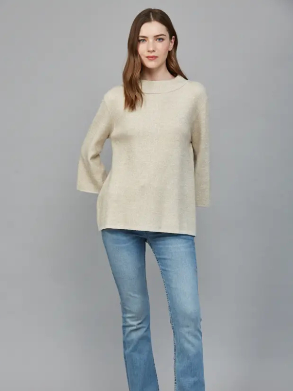 Woman wearing a beige sweater and blue jeans on a gray background
