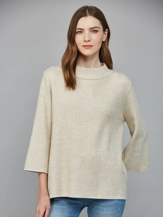 Woman wearing a beige sweater and blue jeans against a gray background
