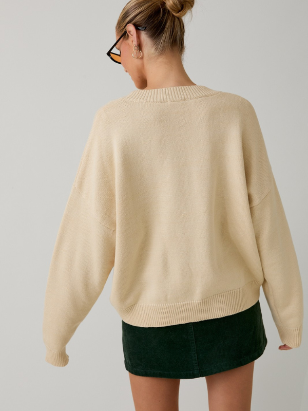 Person wearing a beige sweater and green skirt on a plain background