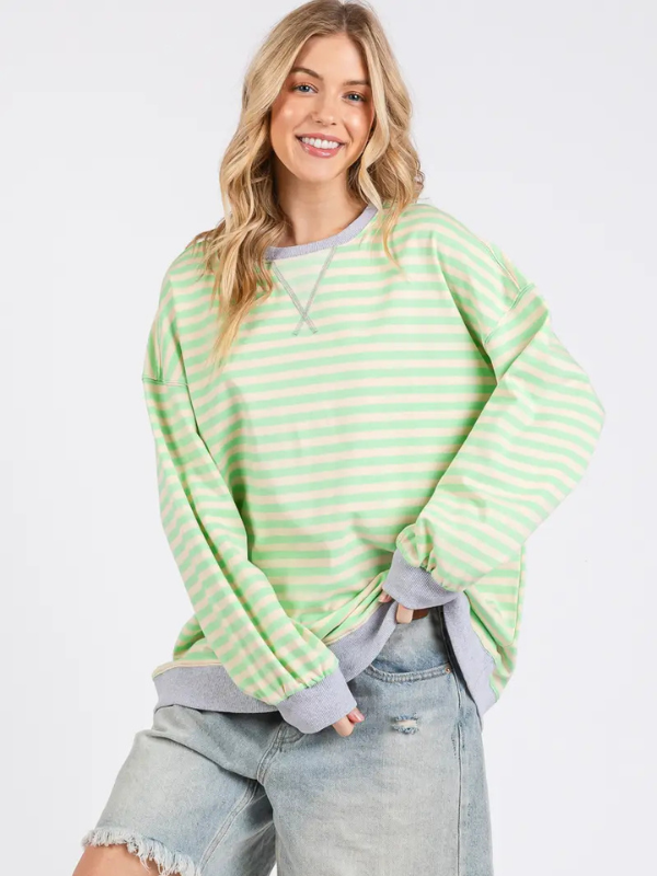 Woman wearing a green and white striped sweater with denim shorts on a light gray background