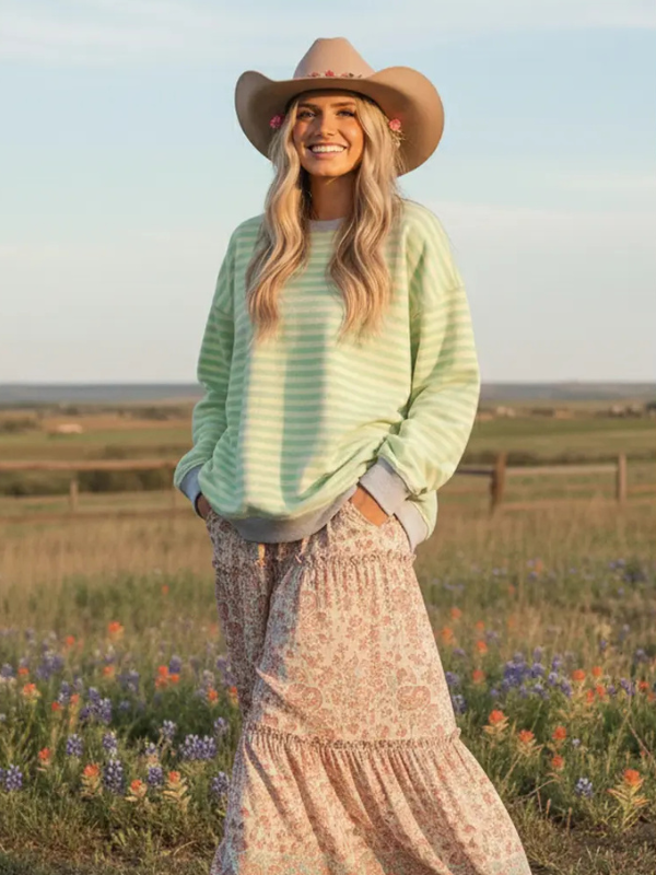 Woman wearing a green striped sweater and wide-brimmed hat in a field with wildflowers.
