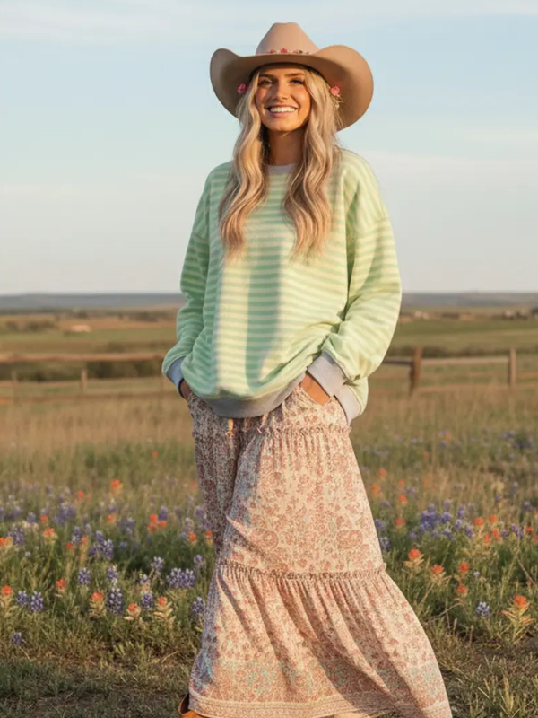 Woman in a green sweater and cowboy hat standing in a field with wildflowers.