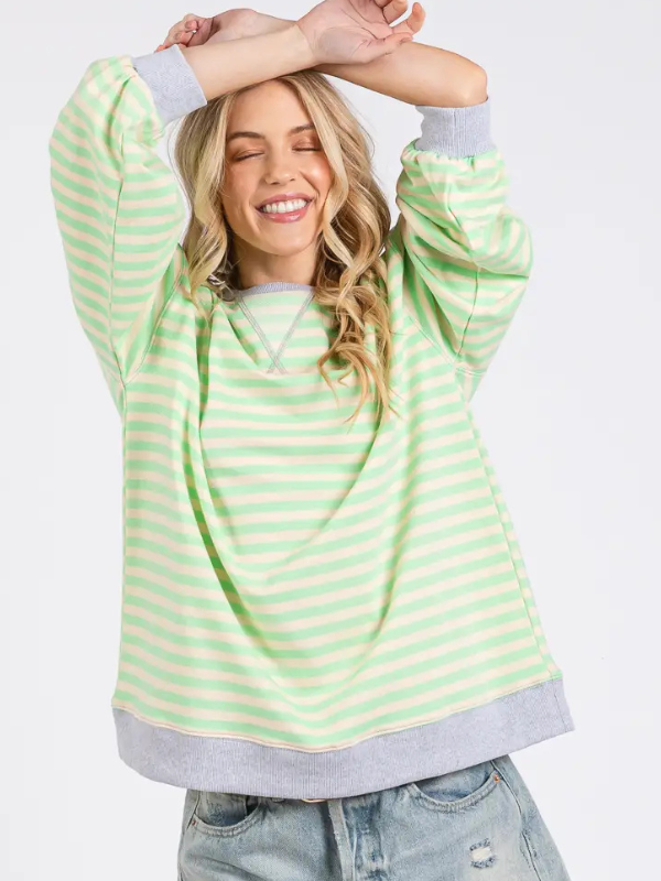 Woman wearing a green and white striped sweater with arms raised on a white background