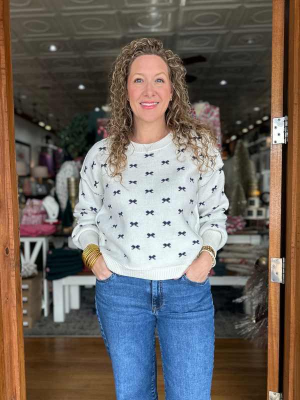 Woman wearing a white sweater with black bow pattern and blue jeans standing in a store.