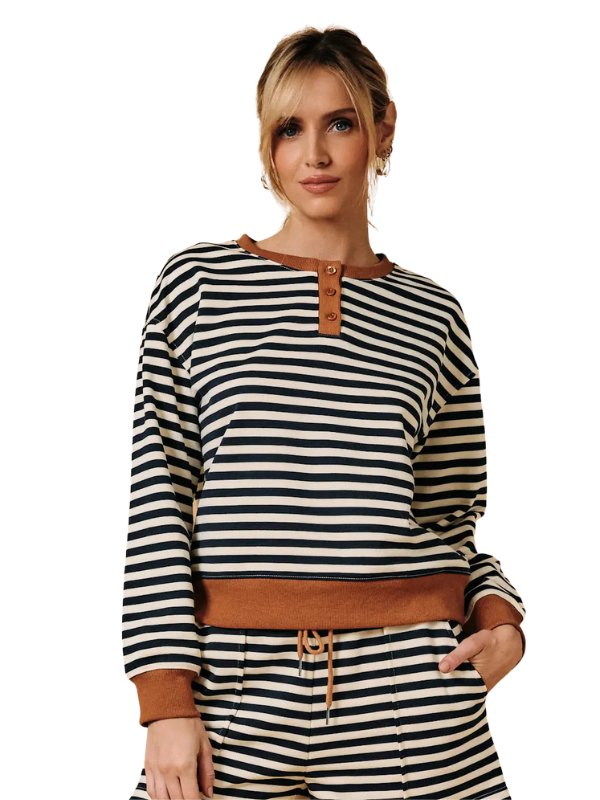 A woman wearing a navy and cream horizontal striped long-sleeve top with brown faux-leather trim, paired with matching striped pants, against a plain white background.