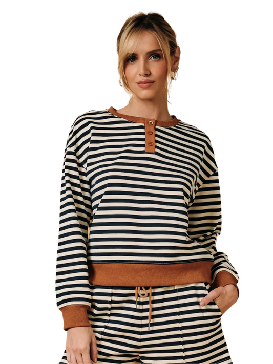 A woman wearing a navy and cream horizontal striped long-sleeve top with brown faux-leather trim, paired with matching striped pants, against a plain white background.
