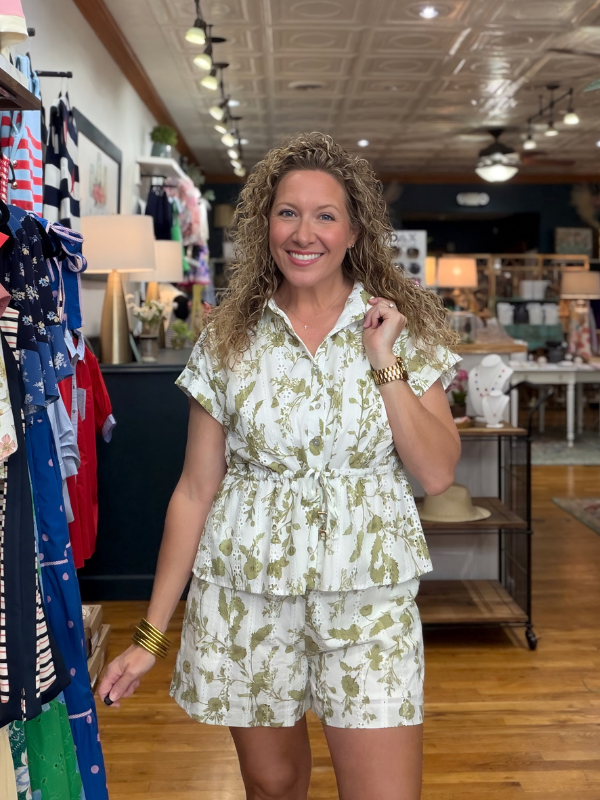 Woman in a floral outfit standing in a store with clothing racks and displays.