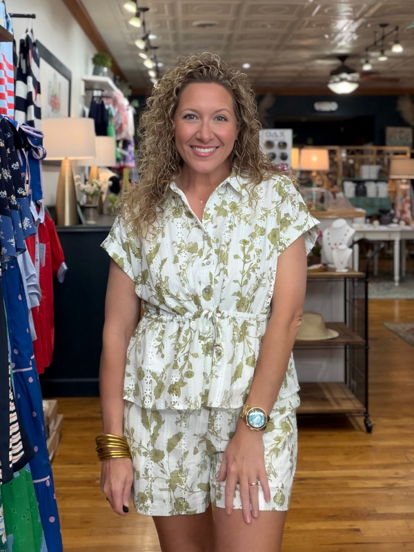 Woman in a floral outfit standing in a store with clothing racks in the background