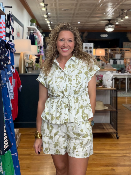 Woman in a floral outfit standing in a store with clothing racks and displays.
