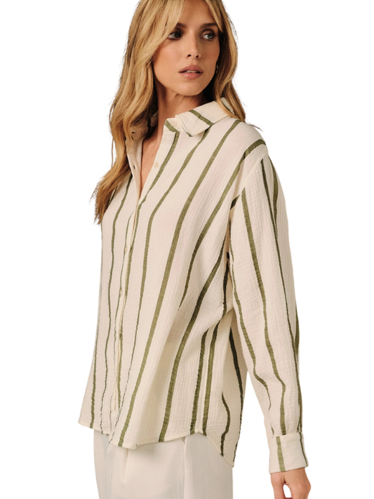 A woman wearing a cream-colored, crinkled long-sleeve button-up blouse with vertical olive green stripes, paired with white pants, against a plain white background.