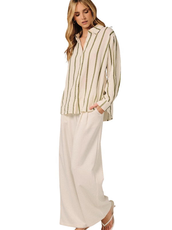 A woman modeling a two-piece outfit featuring a cream and olive green vertically striped long-sleeve button-up shirt and matching cream wide-leg trousers, set against a plain white background.
