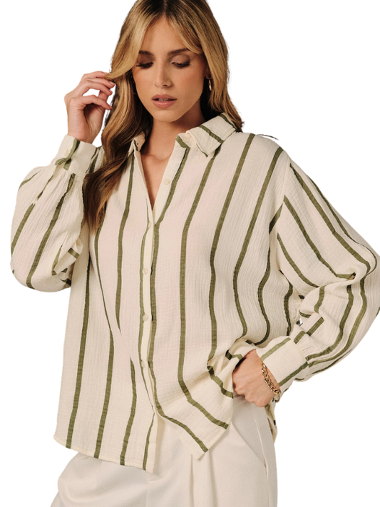 A woman wearing a cream-colored long-sleeve button-up blouse with vertical olive green stripes, paired with cream trousers, against a solid white background.