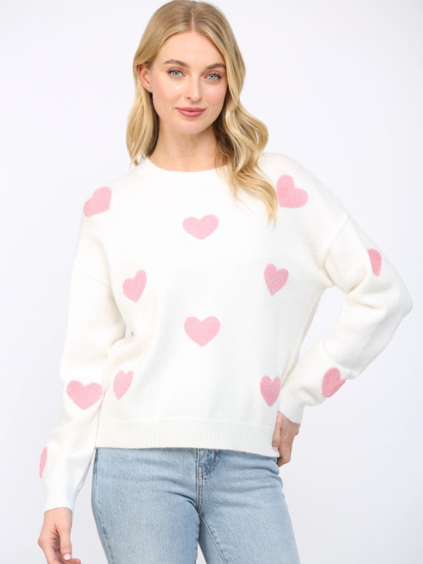 Woman wearing a white sweater with pink heart patterns on a plain background