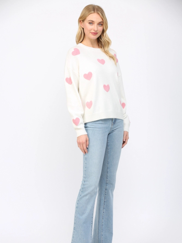 Woman wearing a white sweater with pink heart patterns and light blue jeans on a white background