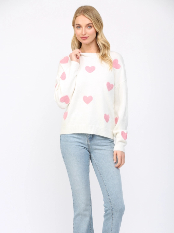 Woman wearing a white sweater with pink heart patterns and light blue jeans on a white background