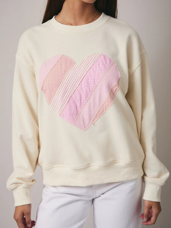 Cream-colored sweatshirt with a pink heart design worn by a person.