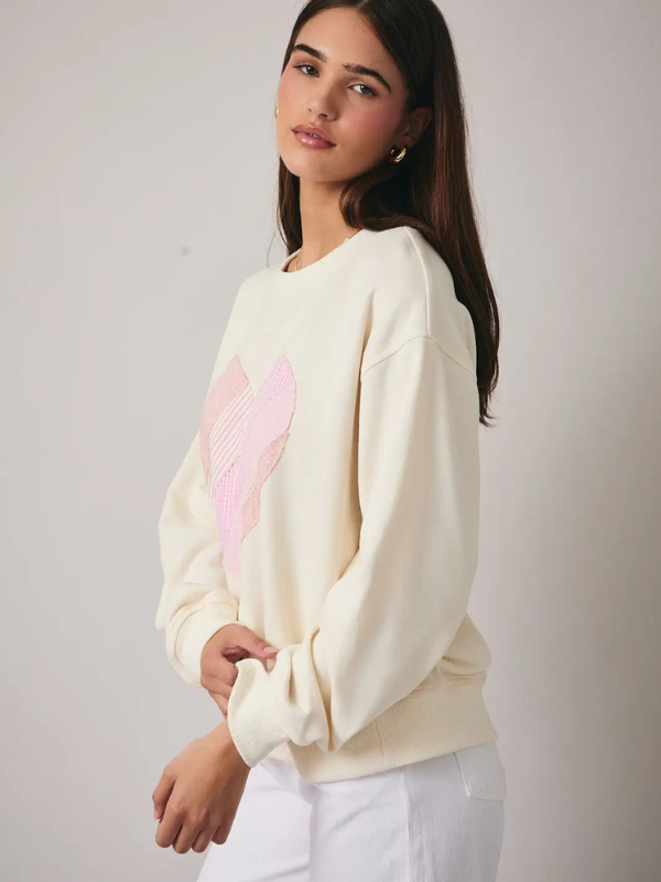 Woman wearing a cream sweater with a pink heart design on a plain background