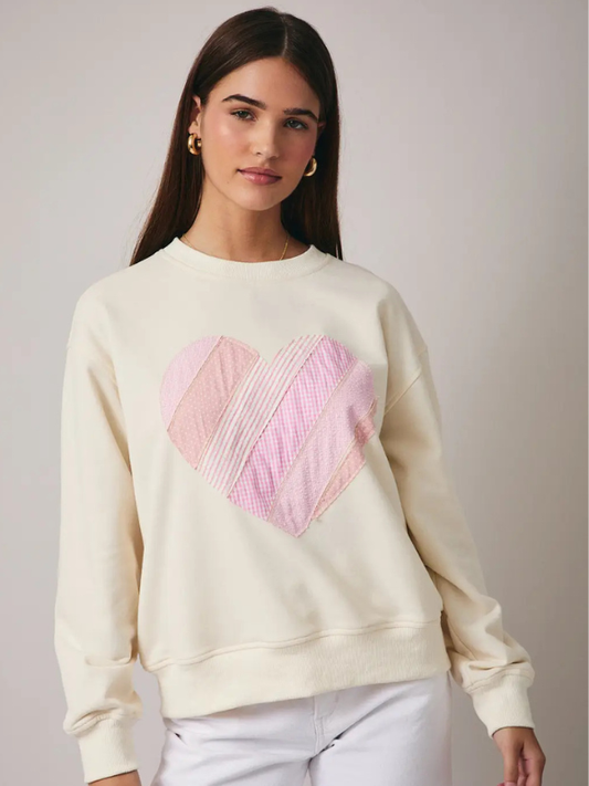 Woman wearing a cream sweatshirt with a pink geometric design on a plain background
