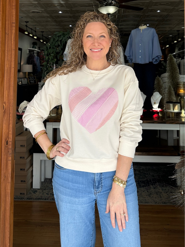 Woman wearing a cream sweatshirt with a pink heart design in a store setting.