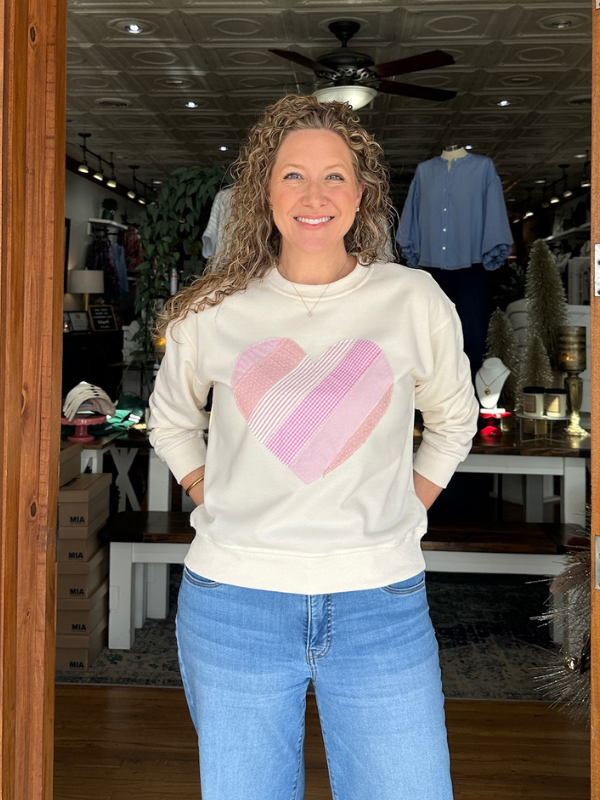 Woman wearing a beige sweatshirt with a pink heart design in a store setting.