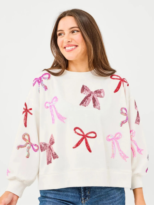 Woman wearing a white sweater with pink and red bow patterns on a light gray background