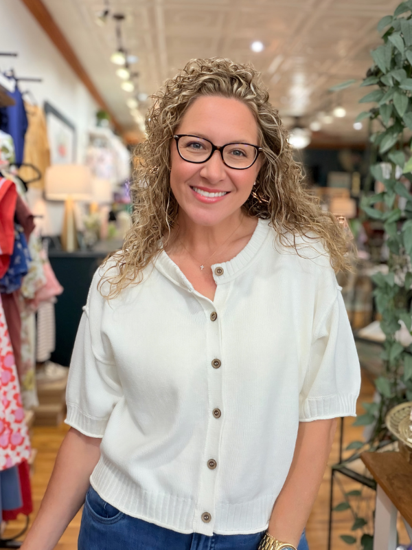 Woman wearing a white cardigan with gold buttons in a store setting