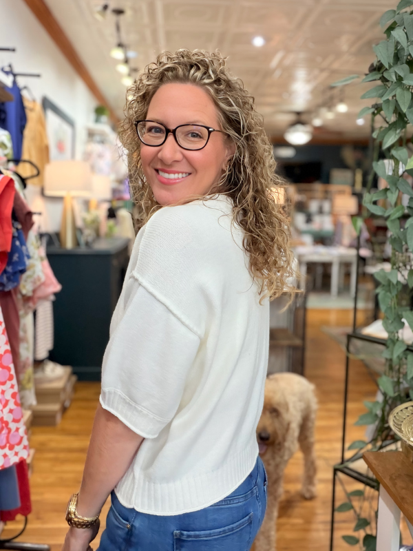 Woman in a store with a dog, wearing glasses and a white sweater.