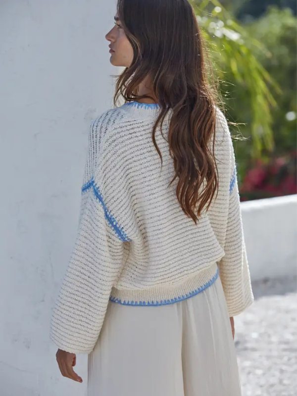 Woman wearing a light-colored knit sweater with blue accents against a white wall.