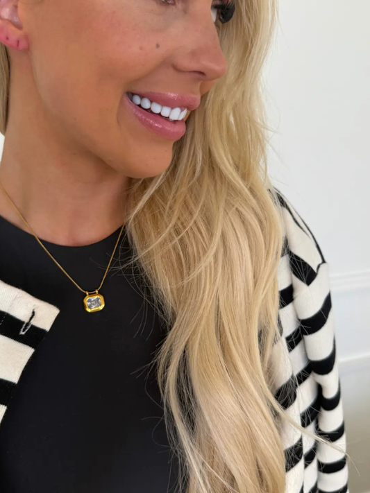 Woman wearing a black and white striped top with a gold necklace featuring a pendant.