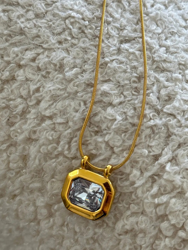 Gold necklace with a clear stone pendant on a textured beige surface