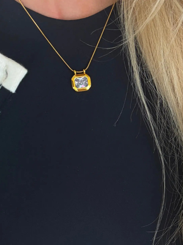 Gold necklace with a diamond pendant worn by a person against a black background