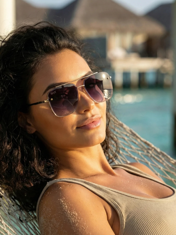 Woman wearing sunglasses and a beige top in a hammock by a waterfront.