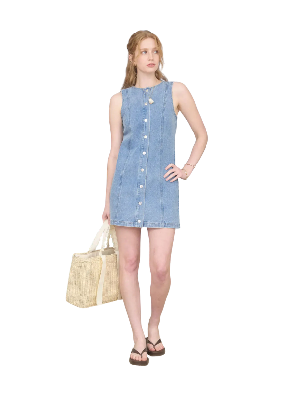 Woman wearing a light blue denim dress holding a beige bag on a white background