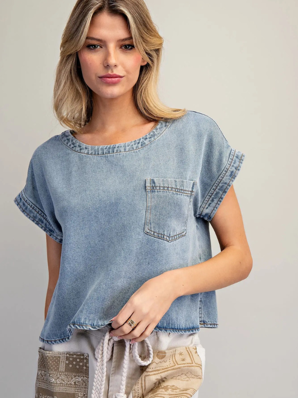 Woman wearing a light blue denim top with a pocket on a plain background
