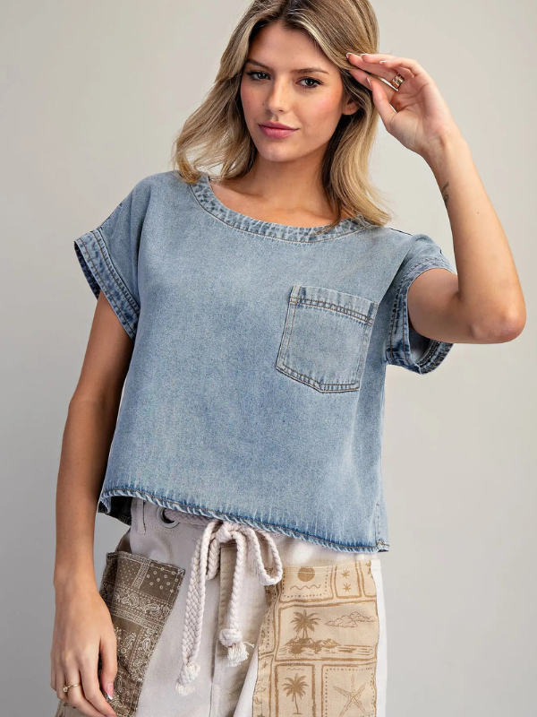 Woman wearing a light blue denim top with a pocket on a gray background