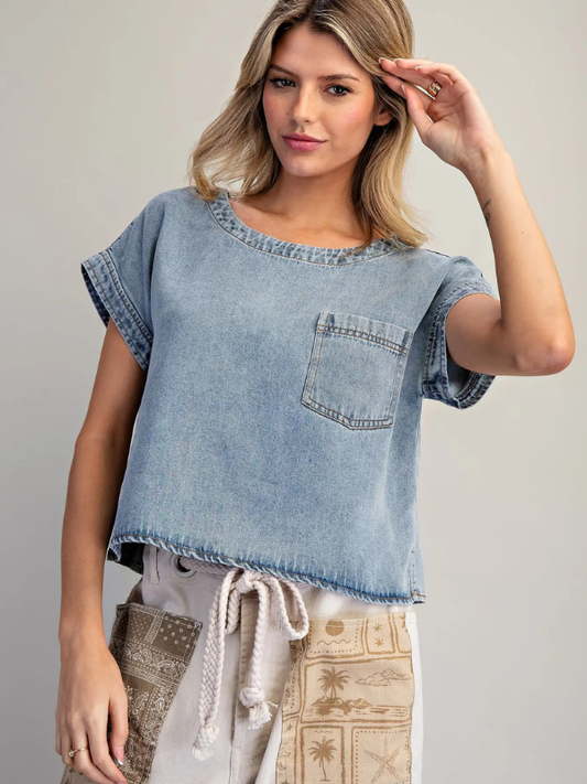 Woman wearing a light blue denim top with a pocket on a gray background