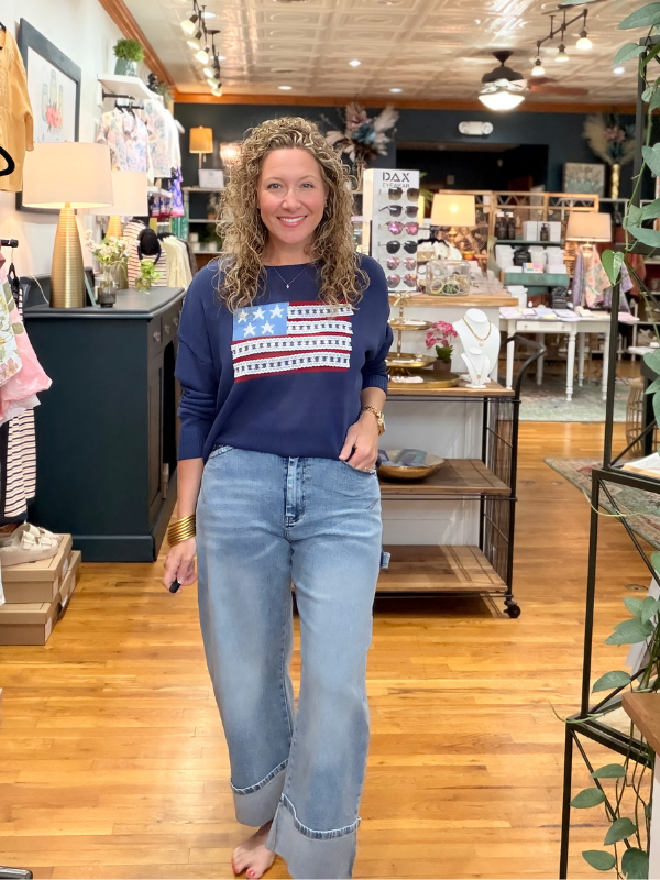 Woman wearing a navy sweatshirt with an American flag design and light blue jeans in a store.