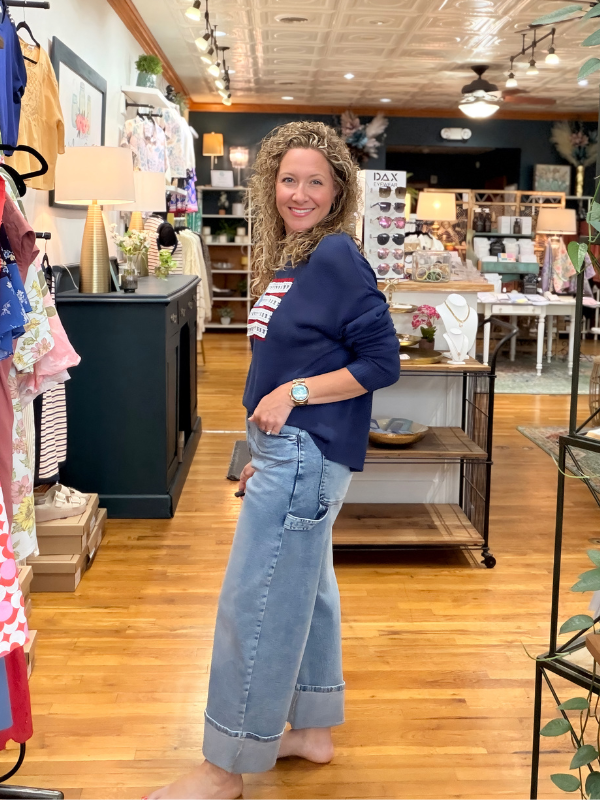 Woman in a store wearing a blue sweater and jeans, surrounded by shelves and products.