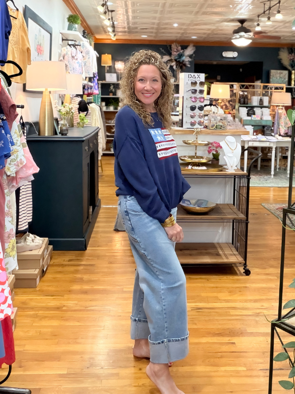 Woman standing in a store with wooden floors and various items on shelves.