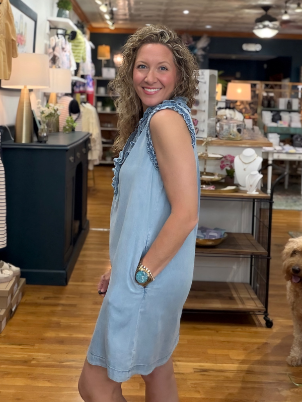 Woman in a blue dress standing in a store with wooden floors and shelves.