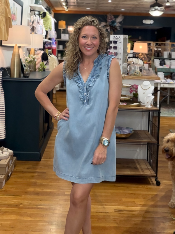 Woman in a light blue dress standing in a store with wooden floors and various items in the background.