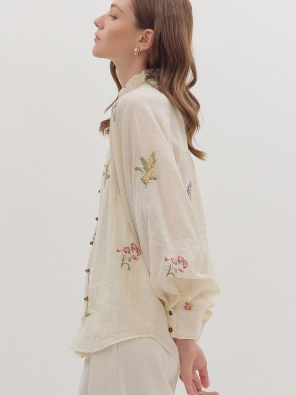 Woman wearing a cream-colored blouse with floral embroidery on a white background