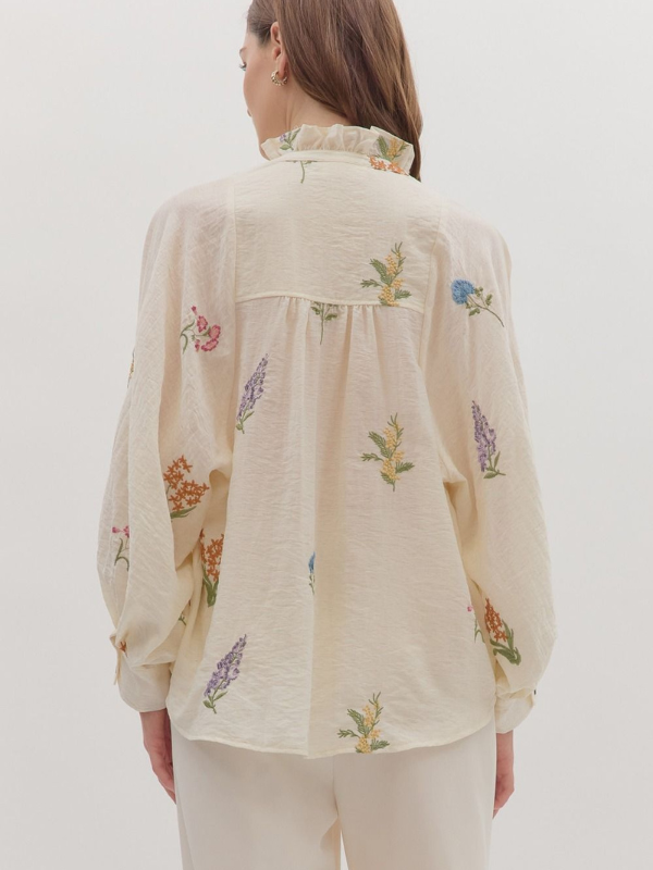 Woman wearing a beige blouse with floral embroidery on a plain background
