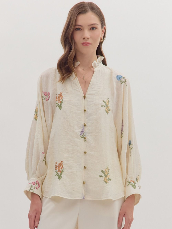 Woman wearing a cream-colored blouse with floral embroidery on a white background