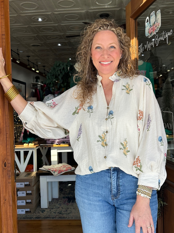 Woman in a floral blouse and jeans standing inside a store.