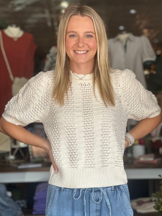 Woman wearing a white textured sweater and blue jeans in a clothing store.