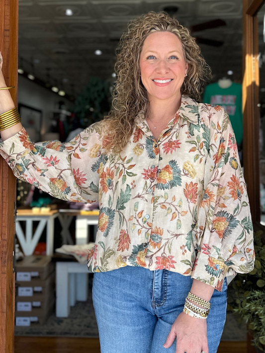 Woman wearing a floral blouse and jeans standing indoors.