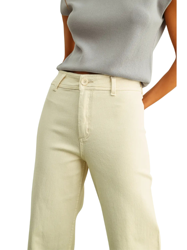A close-up of a model wearing light cream-colored high-waisted straight-leg jeans and a light gray sleeveless top, shown from the chest down against a plain white background.
