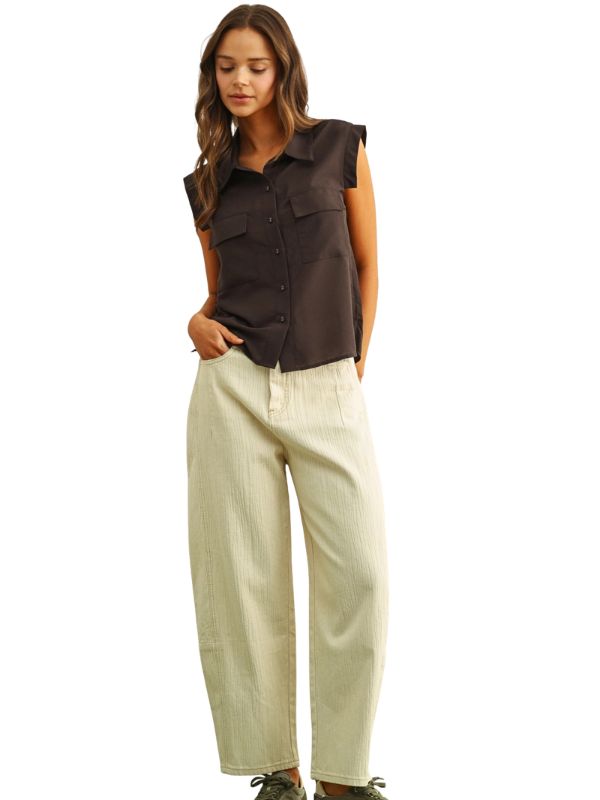 A woman modeling a dark brown sleeveless button-up shirt with ruffled shoulders and light beige wide-leg pants, shown against a plain white background.