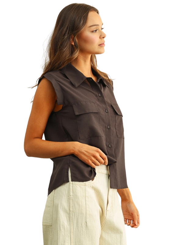 A woman shown in side profile wearing a dark brown sleeveless collared button-front top with flap chest pockets and light cream pants, photographed against a plain white studio background.
